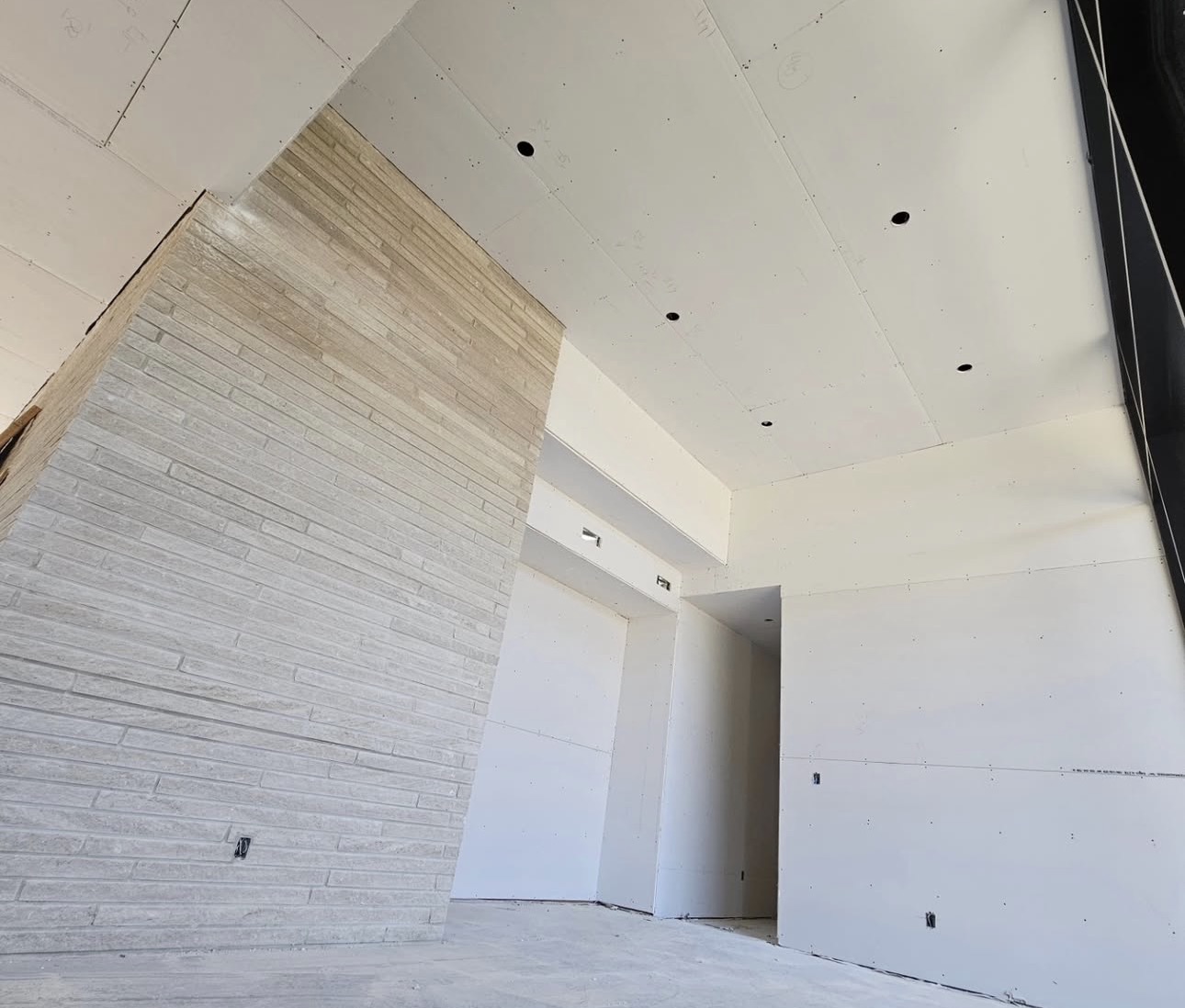 High-ceiling drywall finish with pot lights and accent stone wall