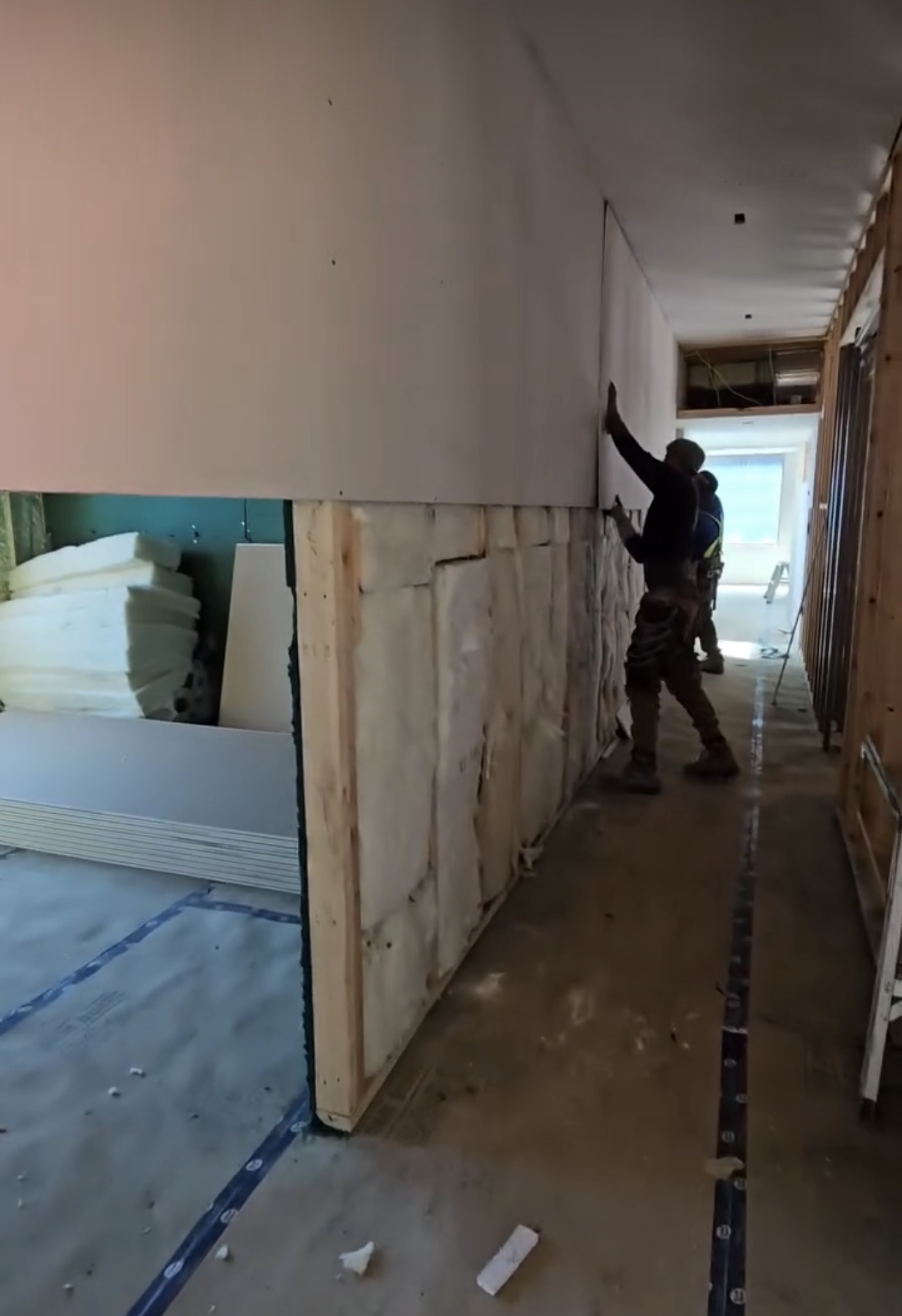 Drywall installer hanging board on framed wall